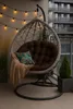 A hanging chair with cushions and a blanket on a balcony, with string lights overhead and plants in the foreground and background. Voir les images du produit