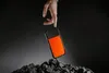 A hand is about to drop an orange and black phone case onto a pile of dark, rough material. Podgląd zdjęcia produktu