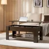 A dark brown lift-top coffee table is shown in a living room setting, with a laptop and mug on its surface, and a sofa in the background. Produktbild-Vorschau