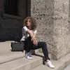 A woman sits on stone steps outdoors with a black handbag next to her. Voir les images du produit