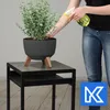 A person is watering a plant in a pot on a table. Náhled obrázku produktu