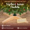 A close-up of the base of an artificial Christmas tree, showing its wooden stand and some ornaments. Produktbild-Vorschau