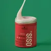 A close-up shot of a red Schwarzkopf Osis+ Texture Thrill elastic fiber gum hair product, with a dollop of the product being pulled out of the container. Podgląd zdjęcia produktu