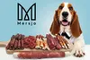A dog wearing a bow tie sits behind a wooden board filled with various dog treats, with a brand logo in the background. Anteprima dell’immagine prodotto