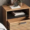 A close-up view of a wooden nightstand with an open drawer, displaying books, glasses, and a clock. Anteprima dell’immagine prodotto