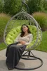 A woman is sleeping in a hanging egg chair outdoors, covered with a blanket. Voir les images du produit