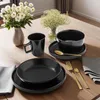 A table setting with black dinnerware and gold cutlery, decorated with flowers. Produktbild-Vorschau