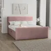 A pink upholstered bed with white pillows and a white cat lying on it, in a bedroom setting with artwork on the wall and curtains in the background. Produktbild-Vorschau