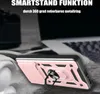 A pink and black phone case with a ring holder is shown on a textured surface, with a blurred laptop in the background. Produktbild-Vorschau