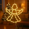 A lit-up angel silhouette decoration hangs in front of a blurred Christmas tree and living room background. Produktbild-Vorschau
