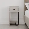 A modern nightstand with a drawer and an open shelf, placed next to a bed in a bedroom setting. The nightstand has a light mocha finish and black metal legs. Produktbild-Vorschau