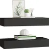 Two black wall shelves are displayed against a white background. The top shelf holds a framed picture of leaves, a potted cactus, and a book. The bottom shelf displays two books and a white decorative vase. Produktbild-Vorschau