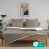 A neatly made bed with taupe bedding and white accents, set against a plain wall with a framed abstract artwork. Produktbild-Vorschau