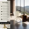 A cream-colored armchair with gold legs is placed in a room with large windows overlooking a scenic mountain landscape. The armchair is positioned near a small side table and a brown ottoman. Produktbild-Vorschau