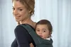 A woman is carrying a baby in a baby carrier on her back. Produktbild-Vorschau
