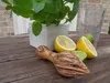 A wooden citrus juicer rests on a rustic wooden table next to halved lemons, lime wedges, and a glass of water with a sprig of mint. Produktbild-Vorschau