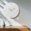 A minimalist wall clock with a marble-like texture and gold hands is displayed on a wall above a wooden cabinet. A small vase with branches sits on the cabinet. Voir les images du produit