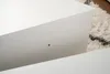 A close-up view of a white piece of furniture, possibly a table or cabinet, with a small dark dot visible on its surface. A fluffy rug with black and white patterns is visible in the background. Produktbild-Vorschau