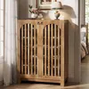 A wooden shoe cabinet with slatted doors is shown in a room setting, with a lamp and flowers on top. A bed is visible in the background. Anteprima dell’immagine prodotto