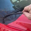 A hand is shown near the hood and windshield of a red car, touching the wiper. Produktbild-Vorschau
