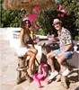 A couple is sitting at a rustic wooden table outdoors, decorated with inflatable flamingos and drinks, suggesting a party or tropical theme. Náhled obrázku produktu