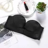 Schwarzer trägerloser BH mit vorderem Clipverschluss, auf weißer Fläche mit Accessoires ausgelegt Náhled obrázku produktu