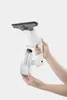 A person's hands are holding a white electric window cleaner with a detachable water tank. Voir les images du produit