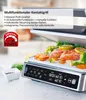 A close-up shot of a multifunctional contact grill with food being cooked on it, featuring a digital display and a promotional overlay. The background shows blurred kitchen elements. Produktbild-Vorschau