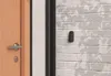 A close-up view of a digital keypad mounted on a brick wall next to a wooden door. Voir les images du produit