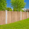 A bamboo privacy screen fence is installed in a garden, with a grassy lawn in the foreground and trees and a house in the background. Produktbild-Vorschau