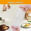 A hand holding a clear plastic bag with red stripes, with kitchen items in the background. Produktbild-Vorschau