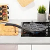 A kitchen counter with a frying pan on a gas stove, a spice rack, and a cutting board. Anteprima dell’immagine prodotto