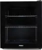 The image shows the front view of a black Primo mini-refrigerator with two wire shelves inside. The door is transparent, allowing a view of the interior. The Primo logo is visible at the bottom center of the unit. Voir les images du produit