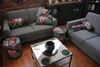 A living room scene with two gray sofas, a coffee table, and two floral-print ottomans. Produktbild-Vorschau