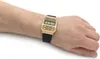 A person's arm and wrist wearing a gold digital watch with a black strap. Anteprima dell’immagine prodotto
