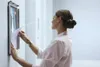 A woman is changing a poster in a frame mounted on a wall. Voir les images du produit