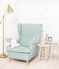 A light blue wingback chair with a white octopus plush toy on the seat, next to two small white side tables. A gold floor lamp is on the left, and a green vase and black alarm clock are on the right table. The background is a white wall with decorative mol Produktbild-Vorschau
