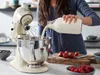 A person pouring milk into a stand mixer bowl, with berries on a cutting board nearby. Produktbild-Vorschau