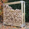 A wooden log store filled with firewood, set outdoors with autumn leaves on the ground and foliage in the background. Produktbild-Vorschau