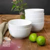 A stack of white bowls and two limes on a wooden table. Produktbild-Vorschau