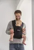 A father is holding his baby in a black baby carrier. Produktbild-Vorschau