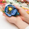 Hands holding a felt flower, with other felt craft supplies in the background. Produktbild-Vorschau