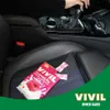 A pack of VIVIL CremeLife Raspberry candies is placed on a car seat, with a person's hand on the gear shift in the background. Produktbild-Vorschau