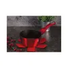 A red saucepan sits on a red trivet on a dark countertop, with dried red petals scattered around. Náhled obrázku produktu