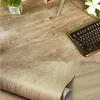 A collage of two images showing a wood-grain patterned adhesive vinyl roll and a close-up of a desk surface with a keyboard and plant. Anteprima dell’immagine prodotto