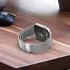 A smartwatch with a silver Milanese loop band is placed on a wooden desk next to a computer mouse. Náhled obrázku produktu