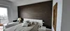 A bedroom with a bed, a large textured wall, and a window overlooking a city. Anteprima dell’immagine prodotto