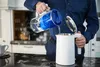 A person is pouring water from a water filter pitcher into a white electric kettle in a kitchen. Produktbild-Vorschau