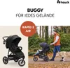 A man pushing a stroller with a dog walking alongside him in a park. Produktbild-Vorschau