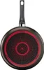 The bottom of a black frying pan with a red and black patterned base and a black handle. Voir les images du produit